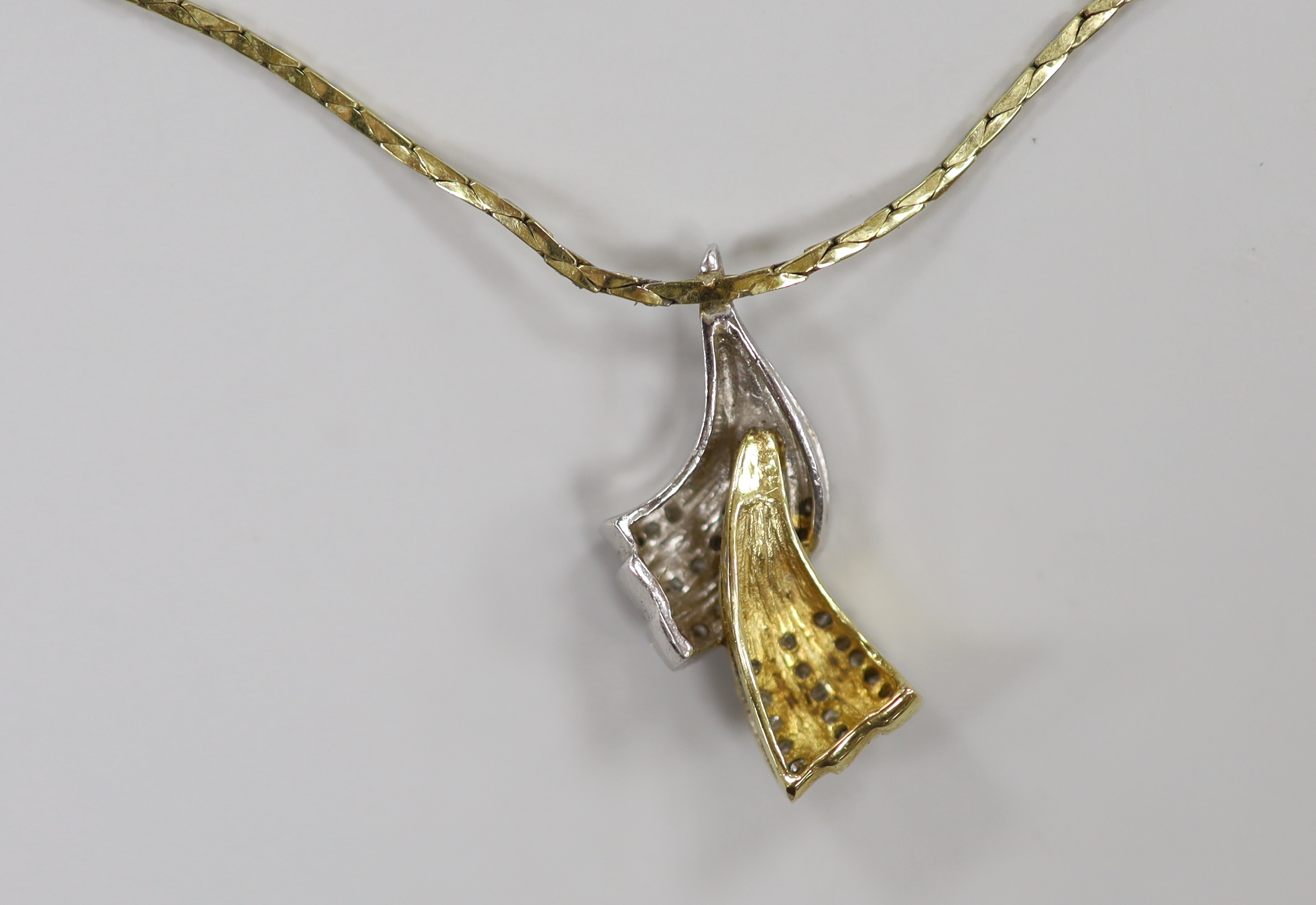 A modern two colour 9ct gold and diamond chip set double scroll pendant necklace, overall 44cm, gross weight 7.4 grams.